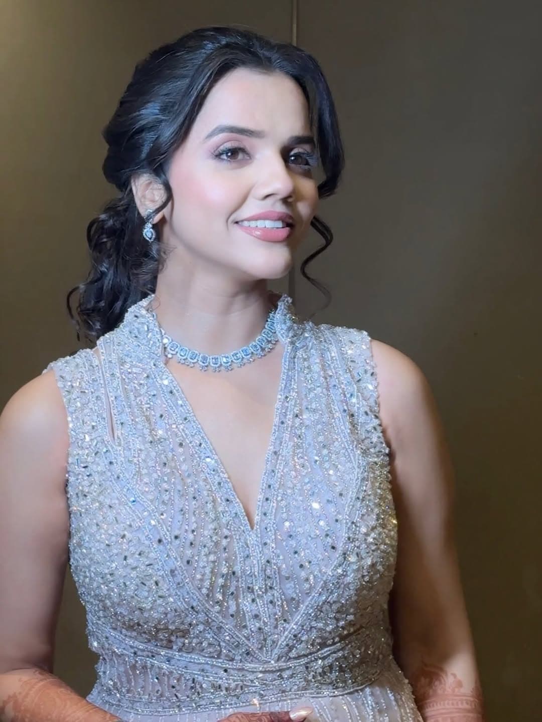 Bridal portrait in a shimmering mauve lehenga with styled waves, chandelier earrings, and intricate henna